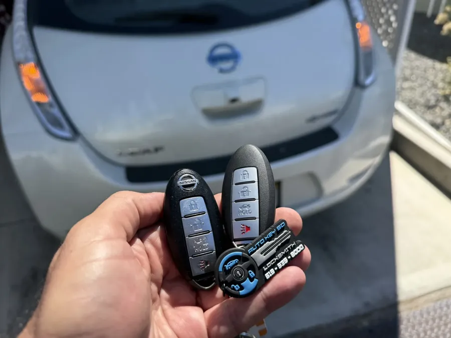 Two Nissan smart keys held behind a Nissan Leaf