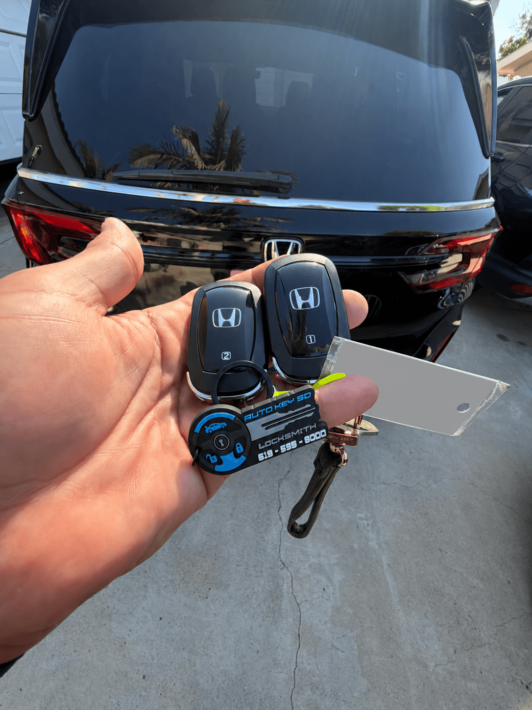 Two Honda key fobs with an Auto Key SD branded tag in front of a Honda Odyssey; customer tag concealed.