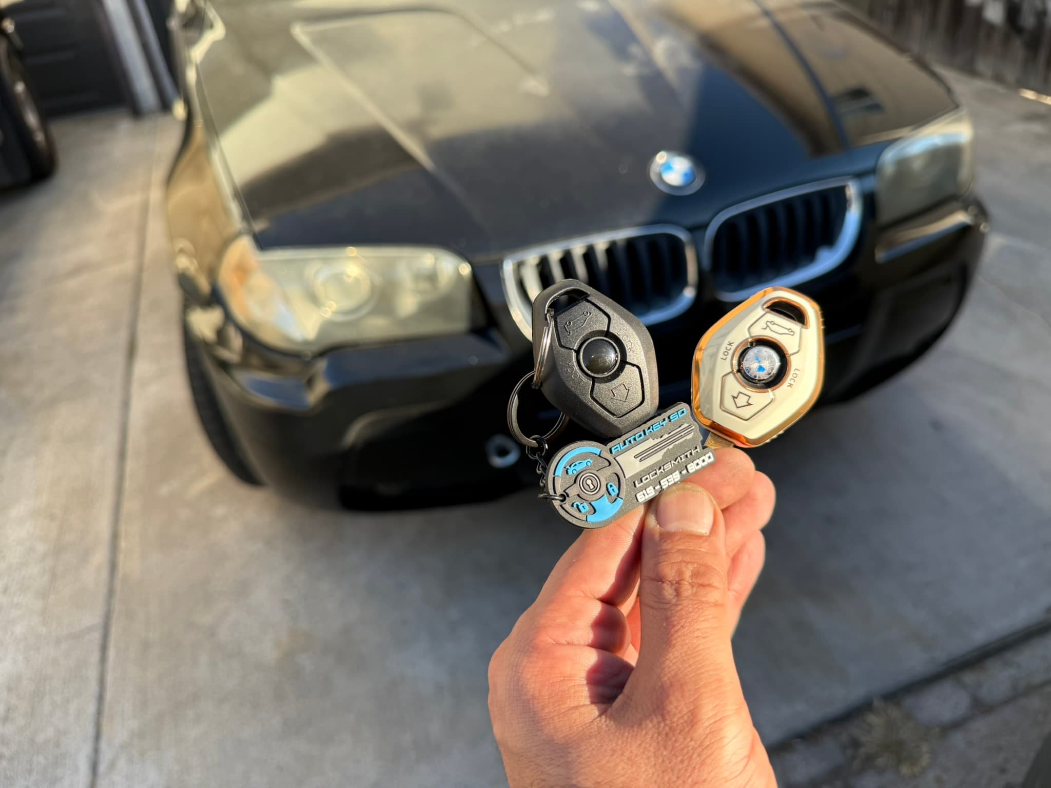 Two remote keys and an Auto Key SD tag held in front of a black BMW
