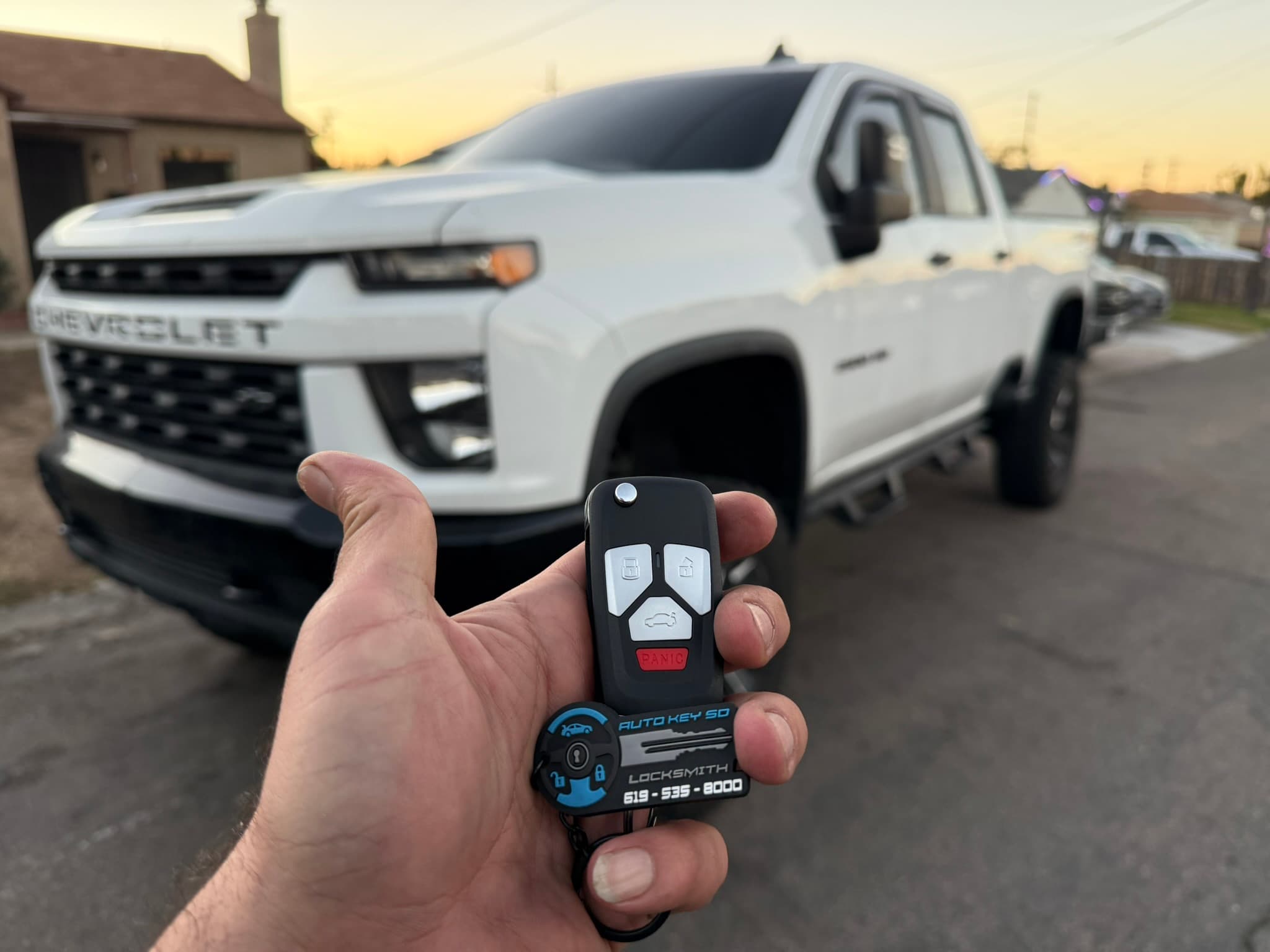 Remote key and Auto Key SD tag held in front of a white Chevrolet pickup