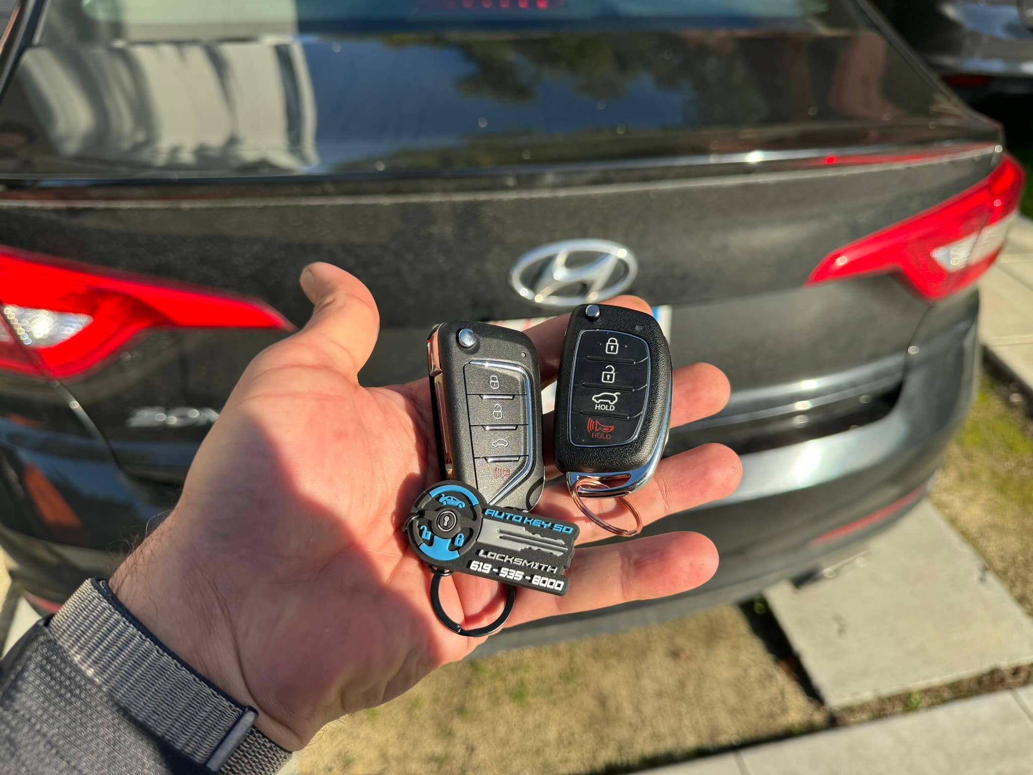 Two remote keys held in front of a Hyundai with an Auto Key SD tag